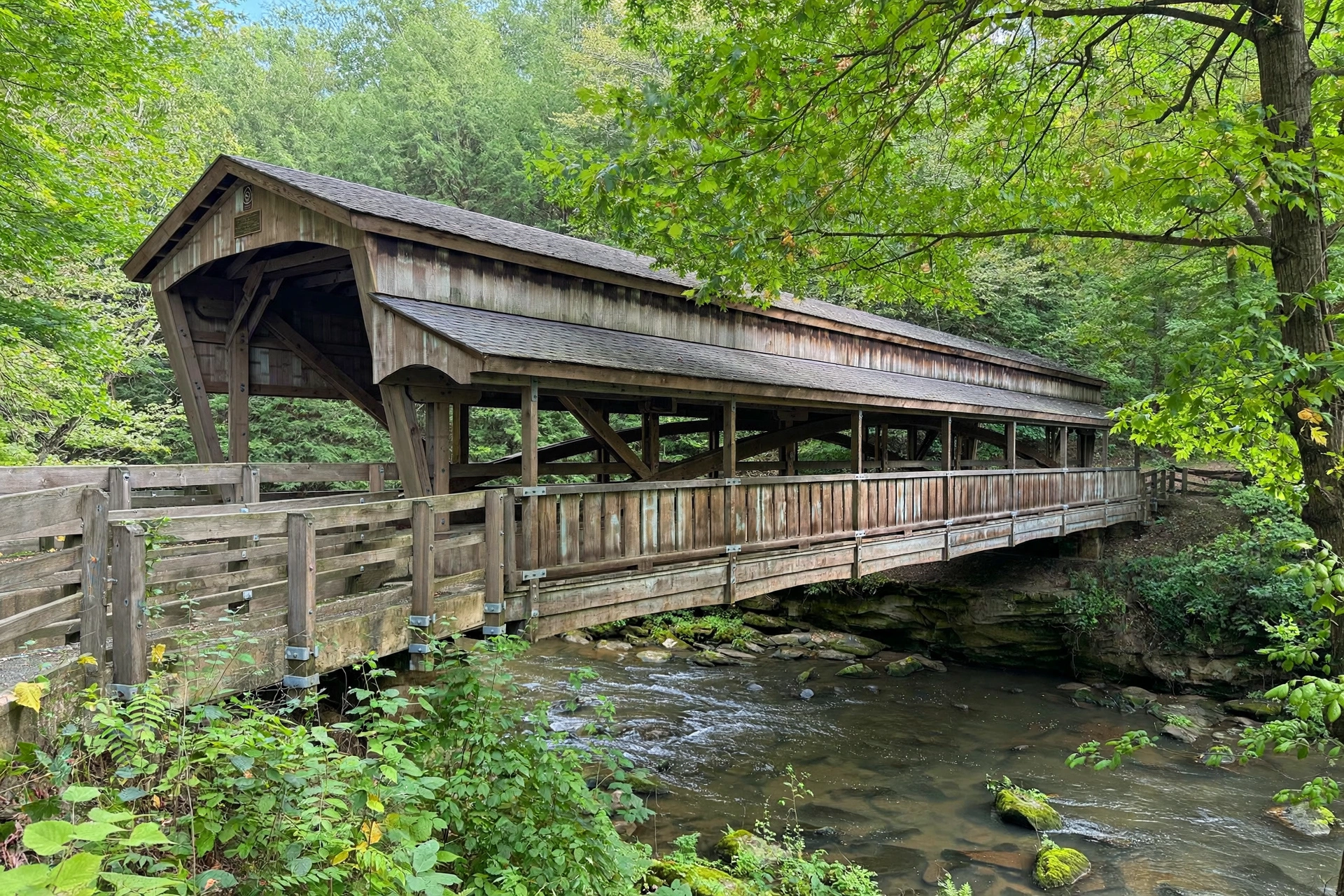 Historic covered wooden bridge over a creek in Mill Creek Park, Youngstown, Ohio, surrounded by green trees